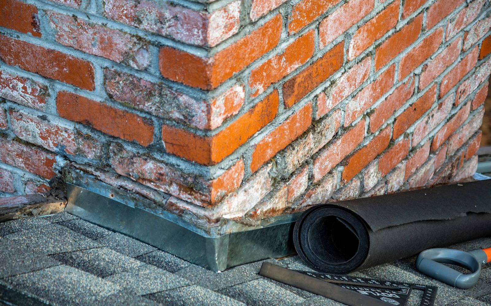 Metal brick flashing installed at the base of a brick chimney